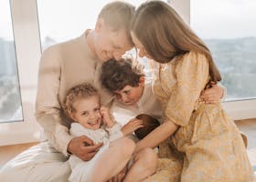 Cheerful family of four cuddling and smiling together in a bright, sunlit living room setting.