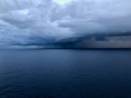 Free A powerful storm approaches over a calm ocean, showcasing dramatic rain clouds and a moody seascape. Stock Photo