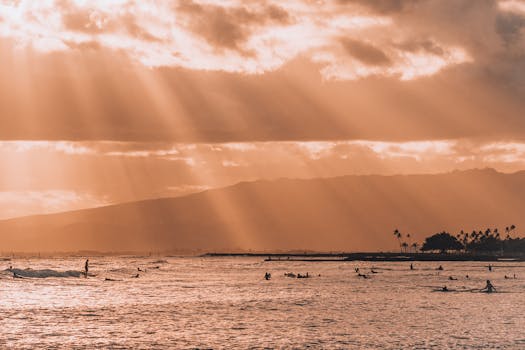 Dramatic rays of sunset light over surfers in Honolulu, Hawaii, creating a vibrant and lively beach scene.