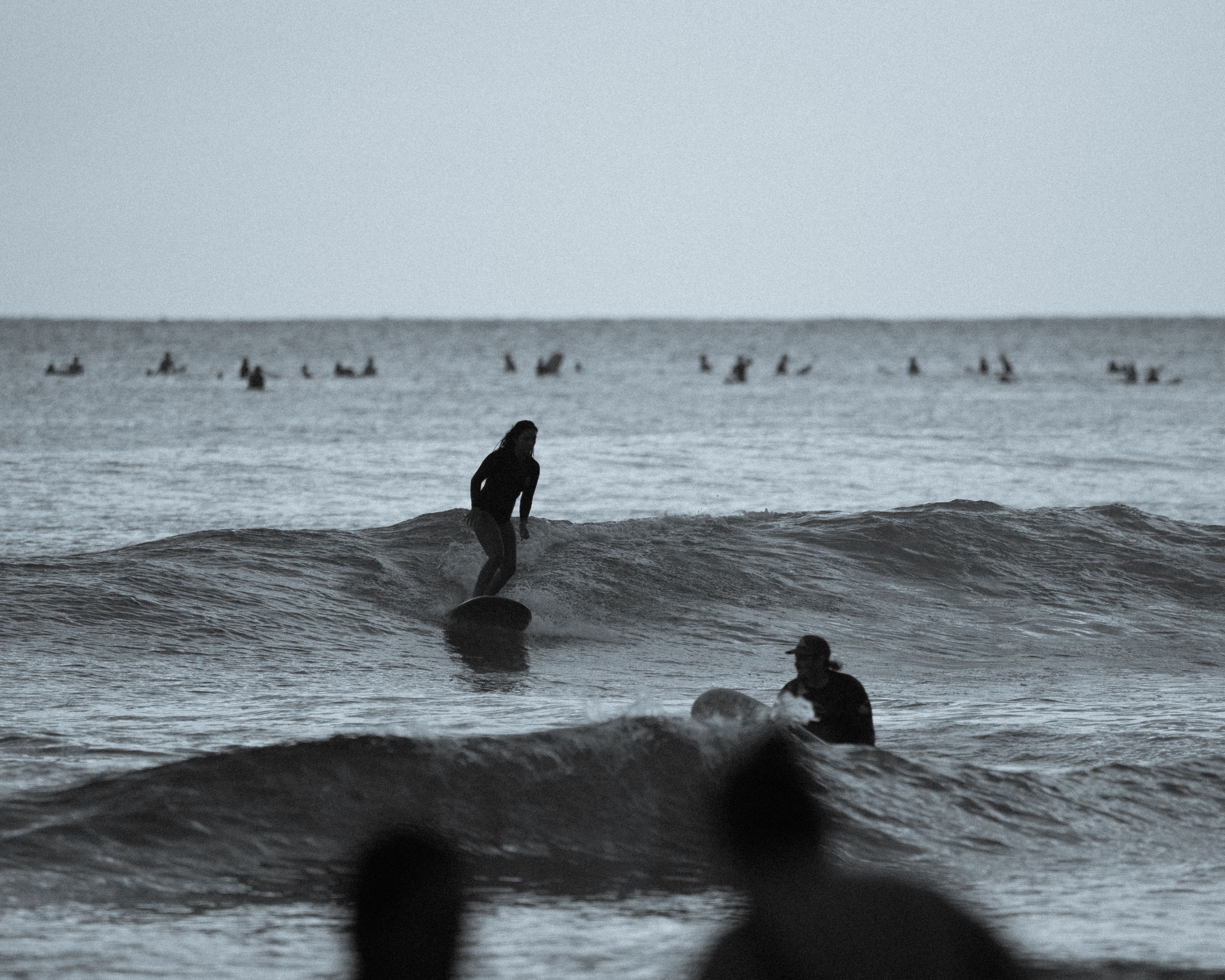 Silhouetted surfers catching waves off the coast of Honolulu, Hawaii at dusk.