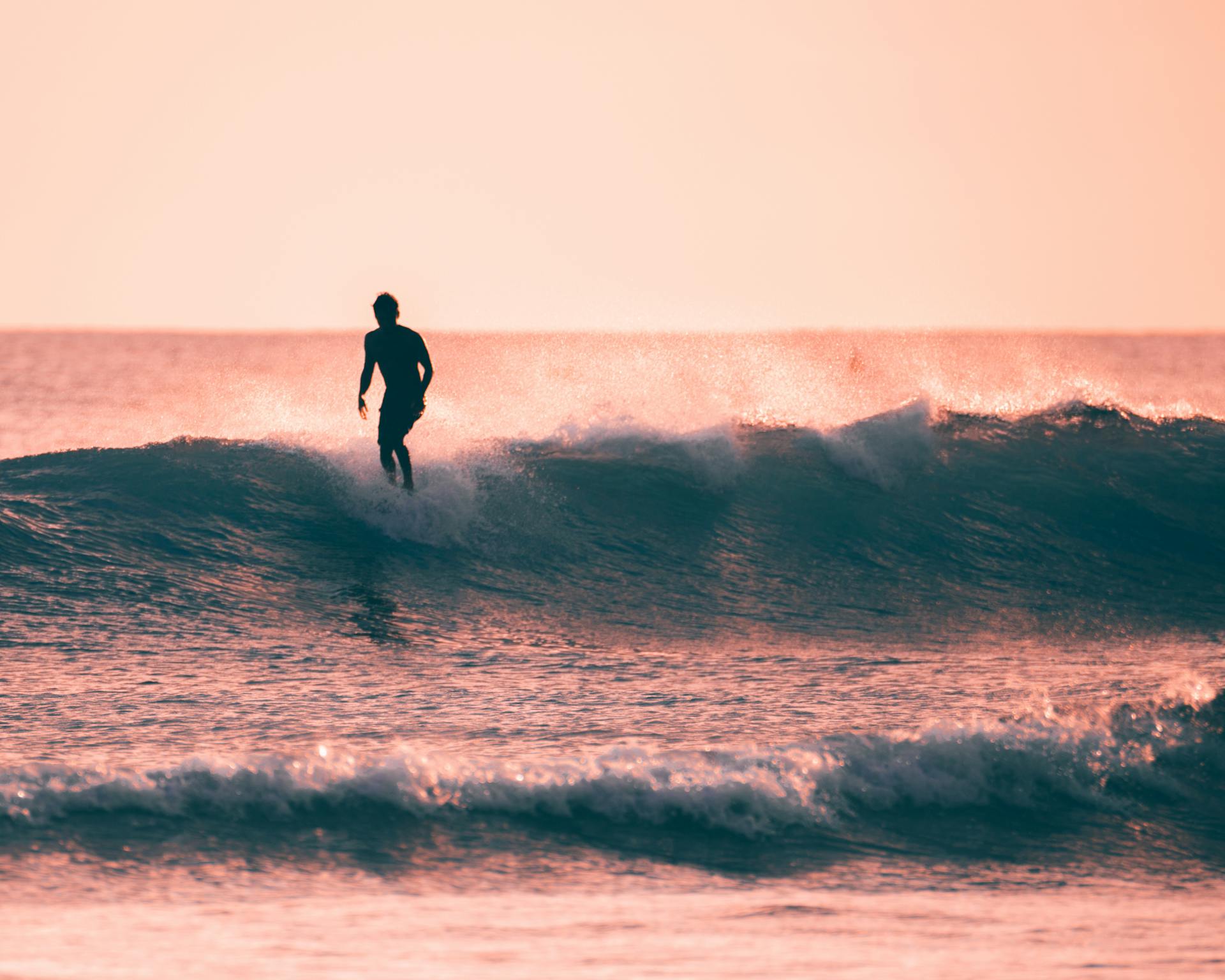 Silhouette of a surfer gliding on waves during a stunning Hawaiian sunset.