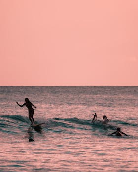 Silhouetted surfers enjoy riding the waves during a stunning sunset in Hawaii.