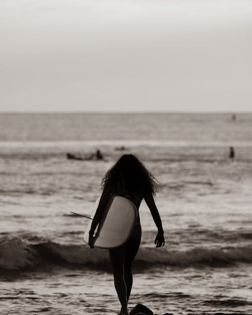 Woman in Black and White Bikini Carrying Surfboard Walking on Beach