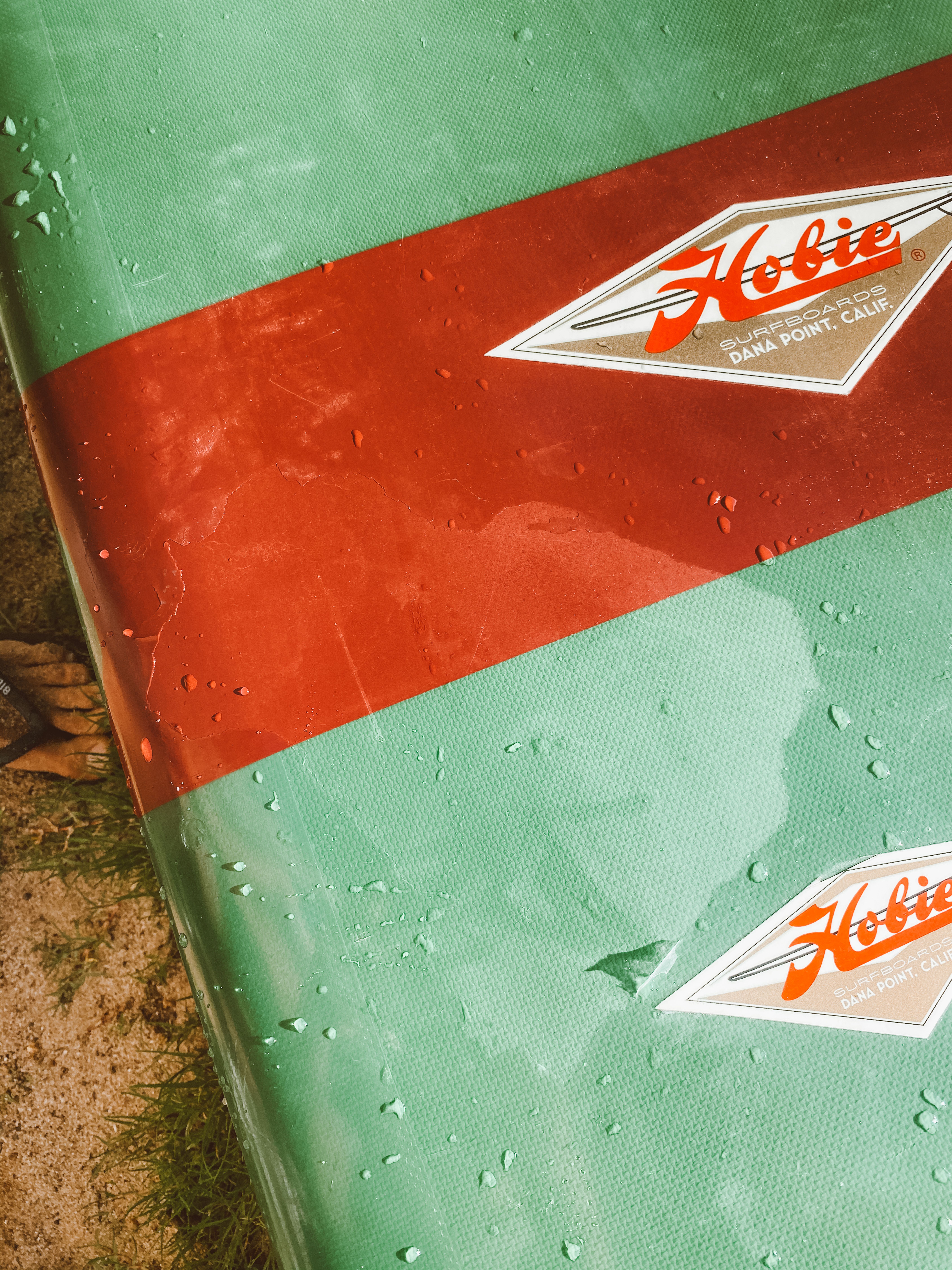Close-up of a vibrant Hobie surfboard with water droplets, perfect for surfing enthusiasts in Hawaii.