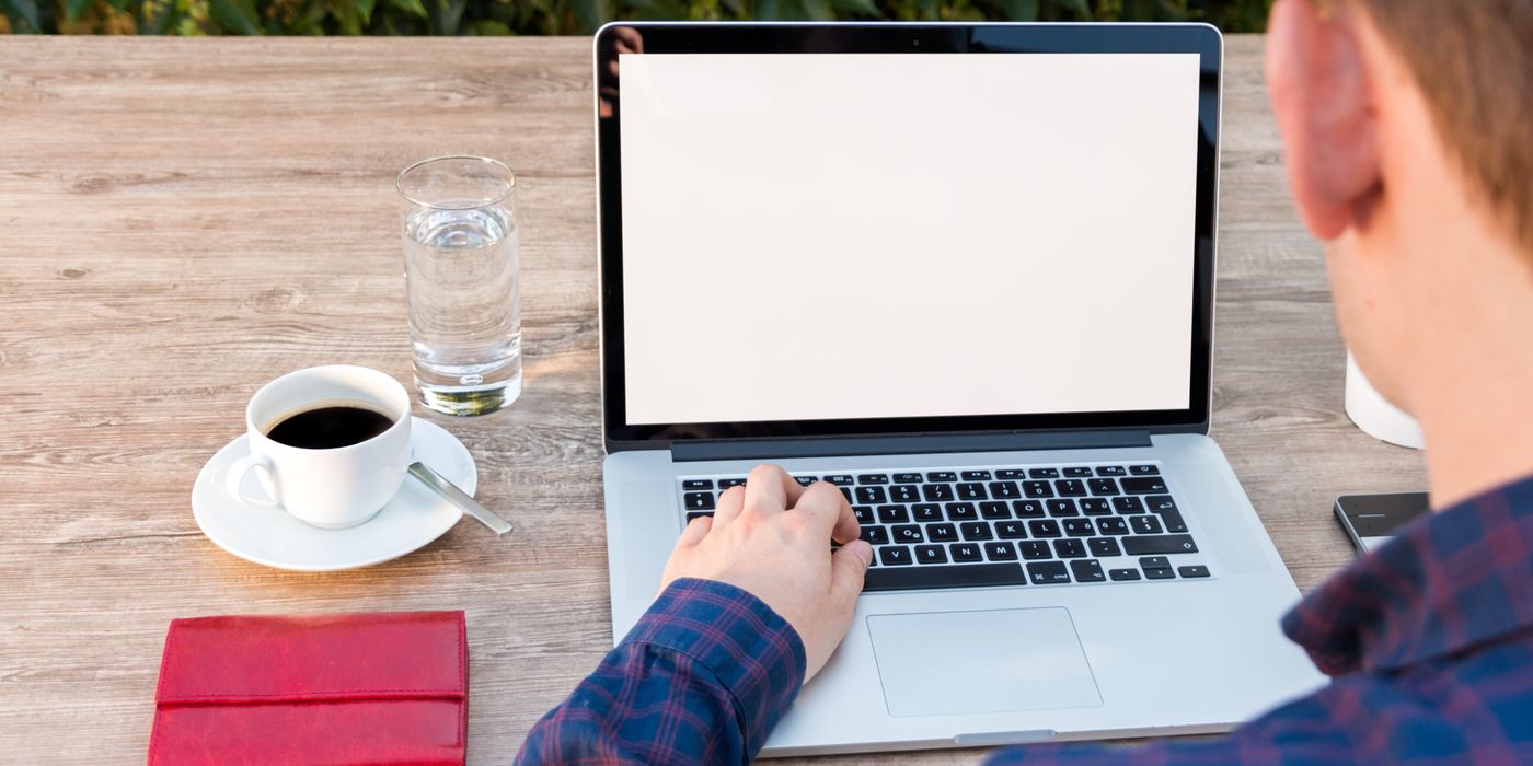 Adult working on laptop outdoors with coffee and notepad, promoting remote work flexibility.