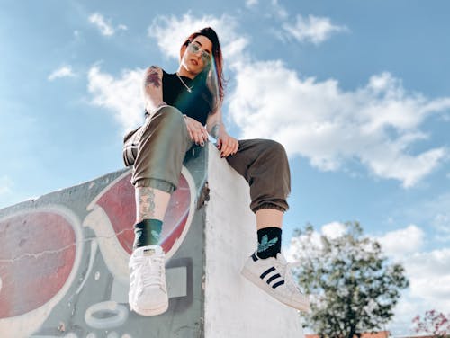 Rebellious tattooed lady relaxing in skate park on sunny day