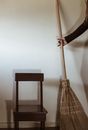 Crop anonymous female holding broom while standing near wooden chair after housework in minimalist room