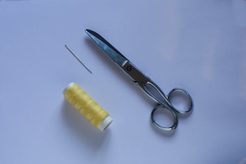 From above of scissors placed on blue table near yellow sewing thread and needle