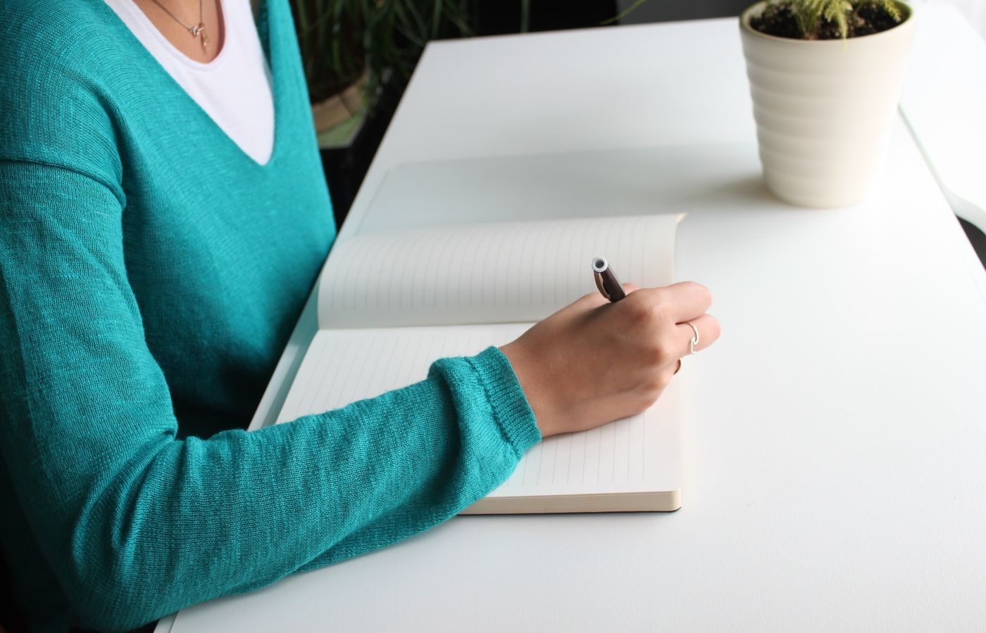 A woman writing in a notebook at a minimalist white desk indoors, emphasizing productivity.