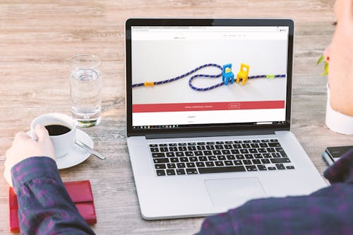 Free Person Holding a Cup of Coffee Beside Macbook Stock Photo