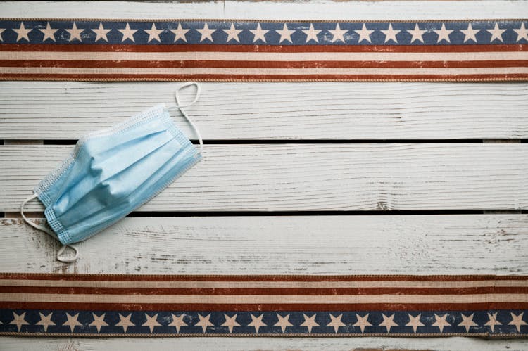 Medical Mask Placed On Wooden Surface With American Flag Ribbon