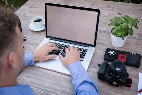 Person Using Macbook Pro Beside Dslr Camera