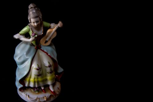 Free Charming porcelain figurine of a woman playing a guitar against a black background. Stock Photo