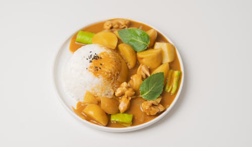 From above of appetizing dish of Indian cuisine curry made of vegetables and meat and served with rice and green leaves