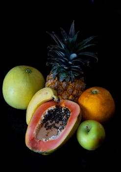 A vibrant display of fresh tropical fruits including papaya, pineapple, orange, and more on a dark background.