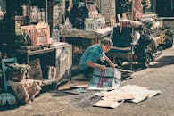 Senior Man in Blue Shirt Sitting on Ground Fixing Old Newspapers