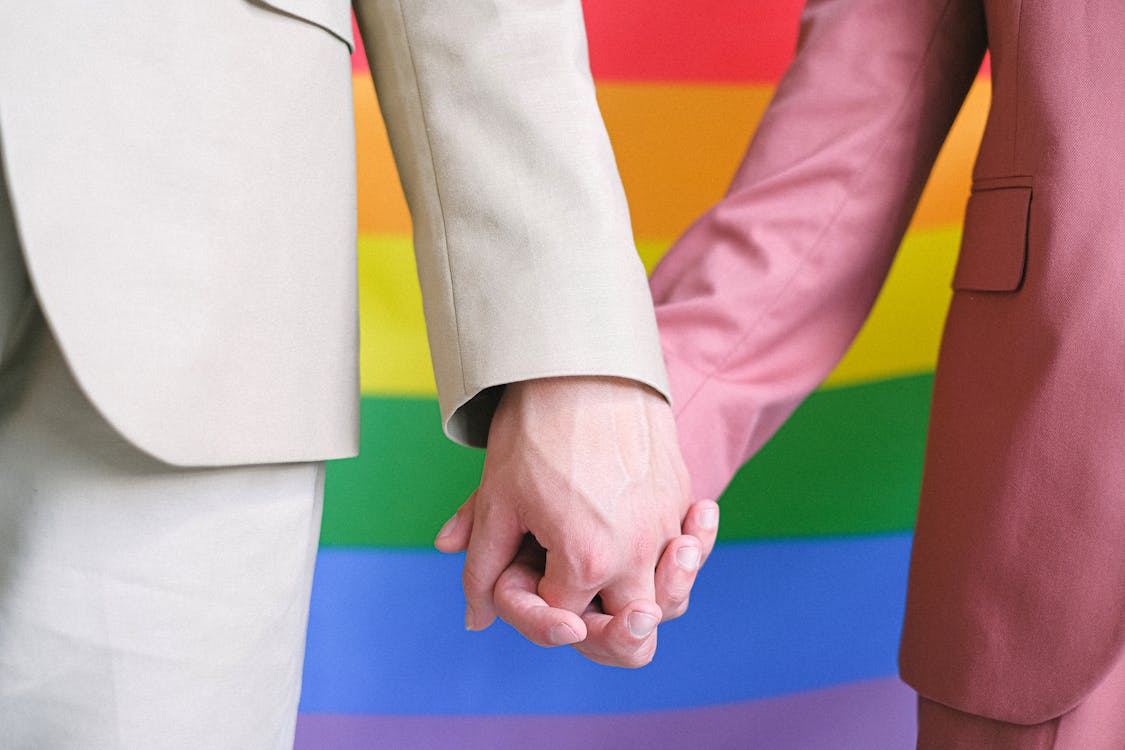 Free Couple Holding Hands in Front of a Gay Pride Flag Stock Photo