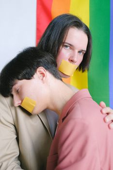 两个年轻人嘴上缠着胶带，在骄傲旗前相拥