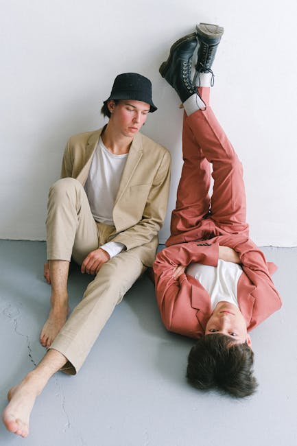 Two young men in stylish suits posing creatively against a white wall.