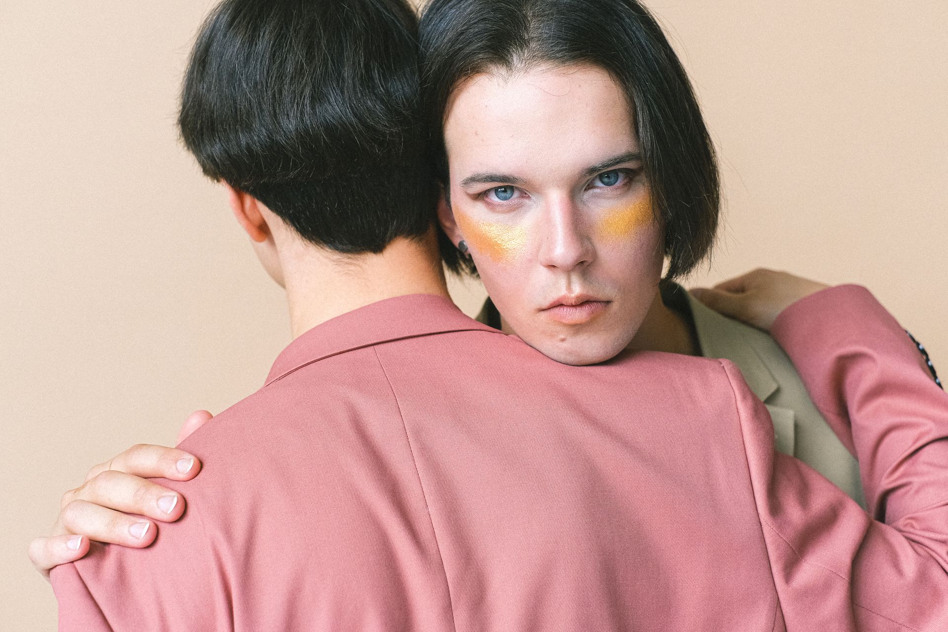 Close-up portrait of two embracing individuals in stylish outfits, showcasing vibrant makeup.
