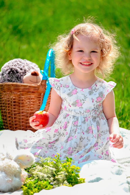 Cute curly haired girl with apple on blanket in nature