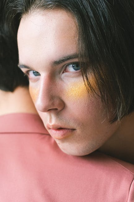 Close-up of a man in a pink suit with artistic makeup, creating a soft and contemplative mood.