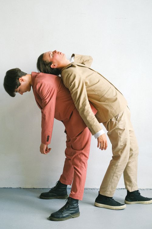 Free Two adults in contrasting suits execute a creative balance pose against a plain background. Stock Photo