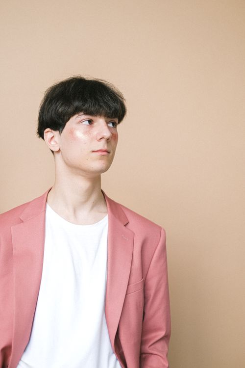 Free Elegant portrait of a young man wearing a pink blazer against a beige background. Stock Photo