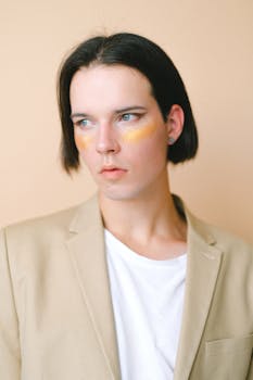 Stylish portrait of a young man with yellow and orange eye makeup and a beige blazer.