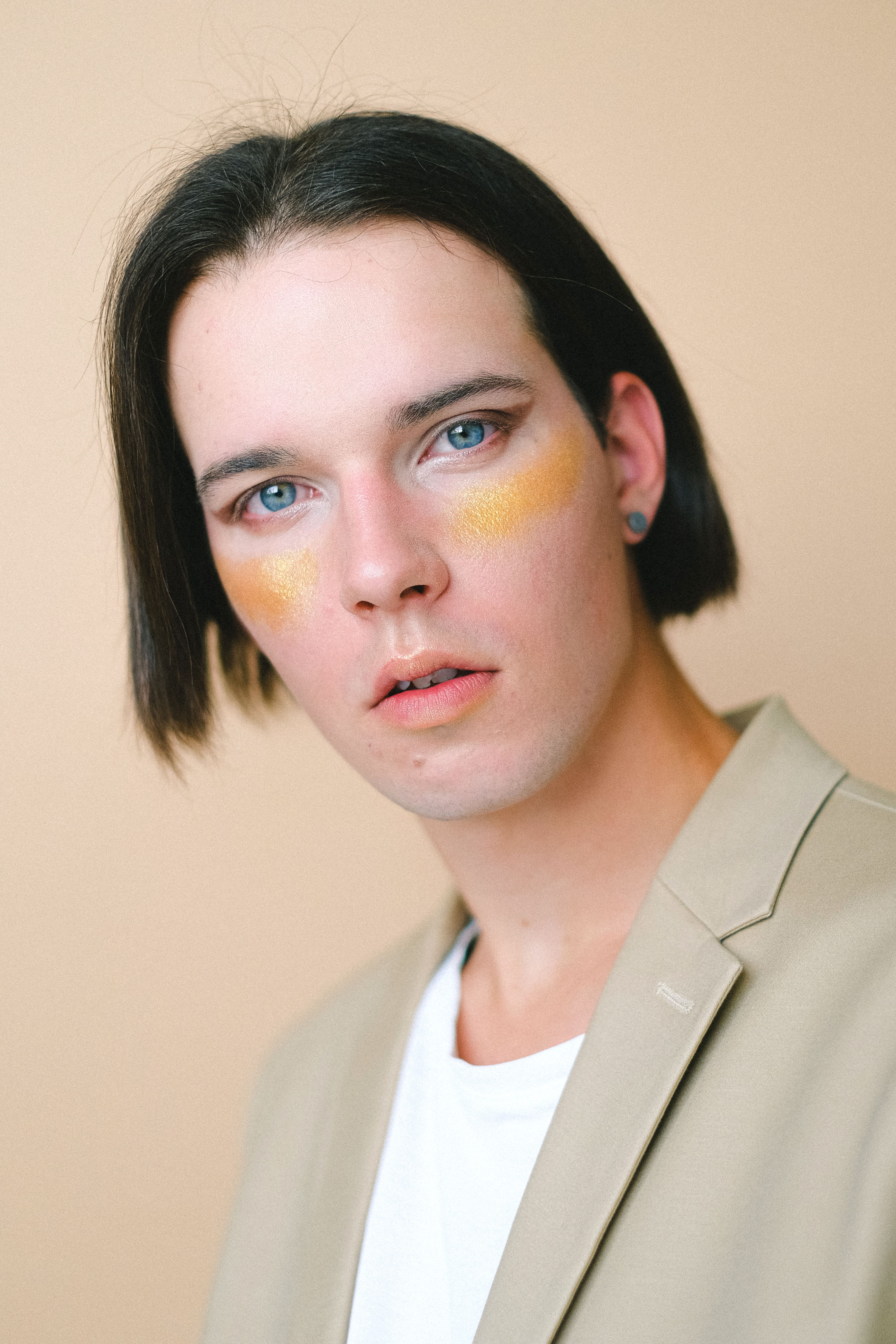 Vibrant portrait of a young adult with artistic eye makeup and beige coat.