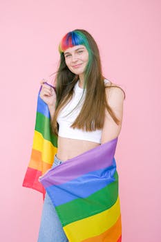 Young woman with rainbow hair holding an LGBT pride flag against a pink background.