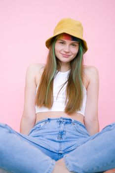 一位穿着休闲服装、头发五颜六色的微笑女人坐在粉红色背景前，散发出欢乐的氛围