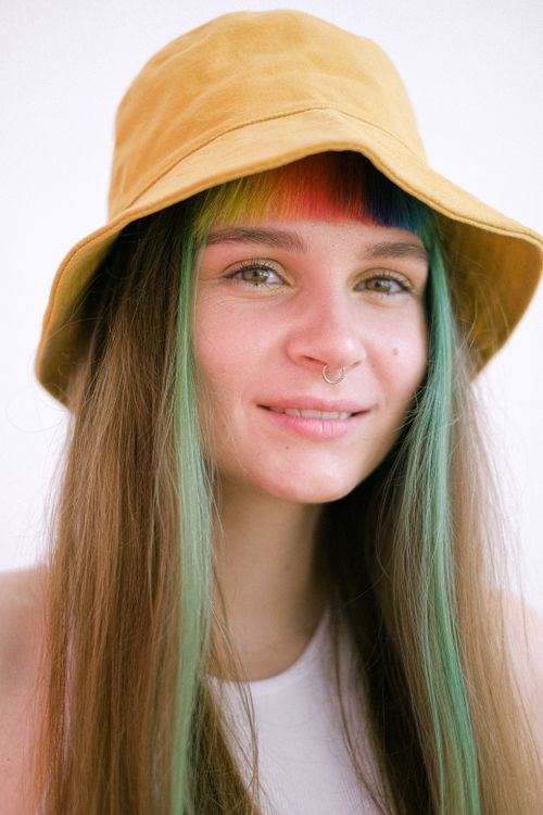 Free Smiling woman wearing yellow hat with colorful rainbow bangs on a white background. Stock Photo