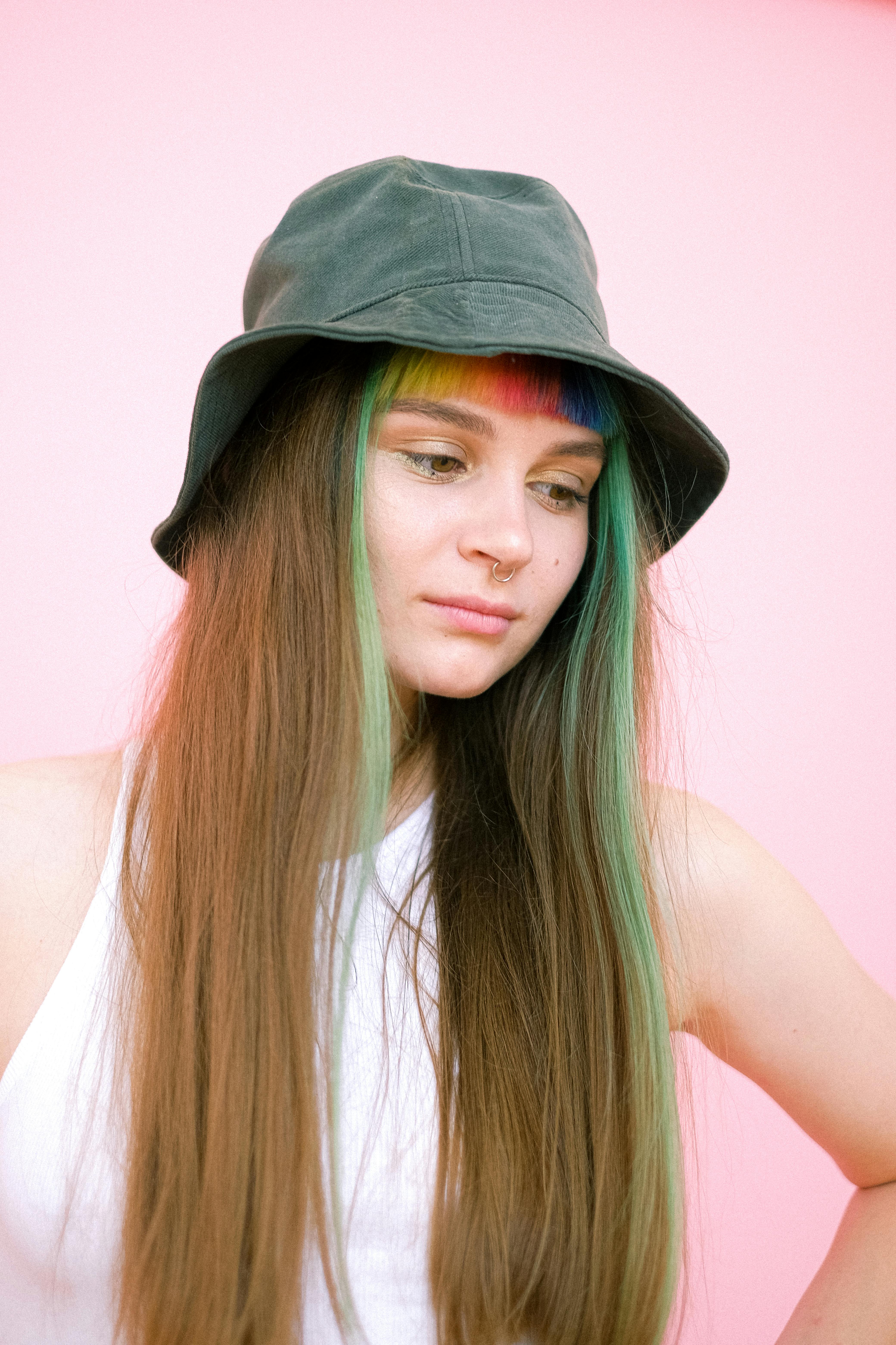 一位女性的创意肖像，彩虹染发，头戴帽子，背景为粉红色