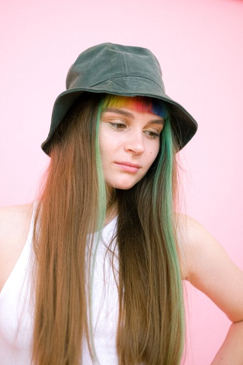 Free Creative portrait of a woman with rainbow-dyed hair and a hat on a pink background. Stock Photo