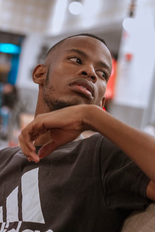 African American unshaved man in t shirt sitting on couch and thoughtfully looking away