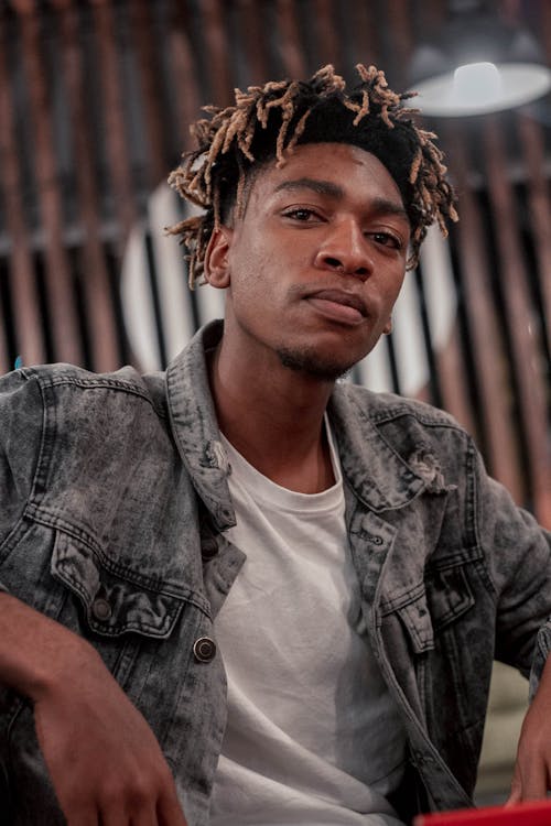 Low angle of serious African American male in denim jacket and white t shirt confidently  looking at camera