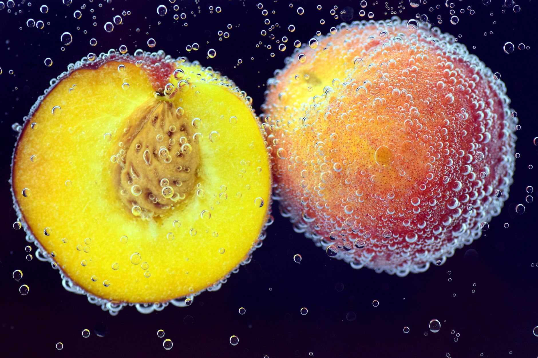 Close-up of ripe peaches submerged in water with air bubbles, highlighting freshness and vibrant color.