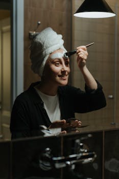 A woman in a bathroom applies a facial mask, embracing self-care.