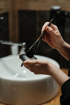 Woman's hands holding a makeup brush in bathroom, depicting a beauty routine.
