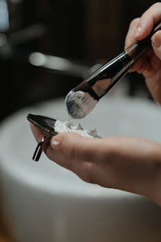 A detailed close-up shot of a hand using a brush to apply face cream on a pad, highlighting self-care routines.