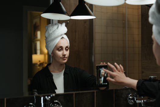 A woman with a towel on her head takes a selfie in a stylish bathroom mirror.