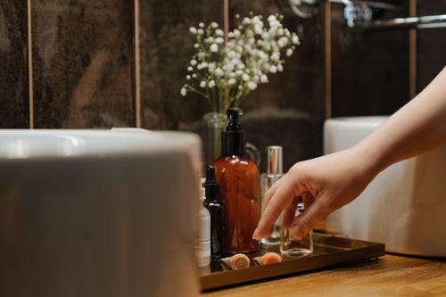 Free A stylish bathroom scene featuring cosmetics and skincare products on a tray with a hand reaching for them. Stock Photo