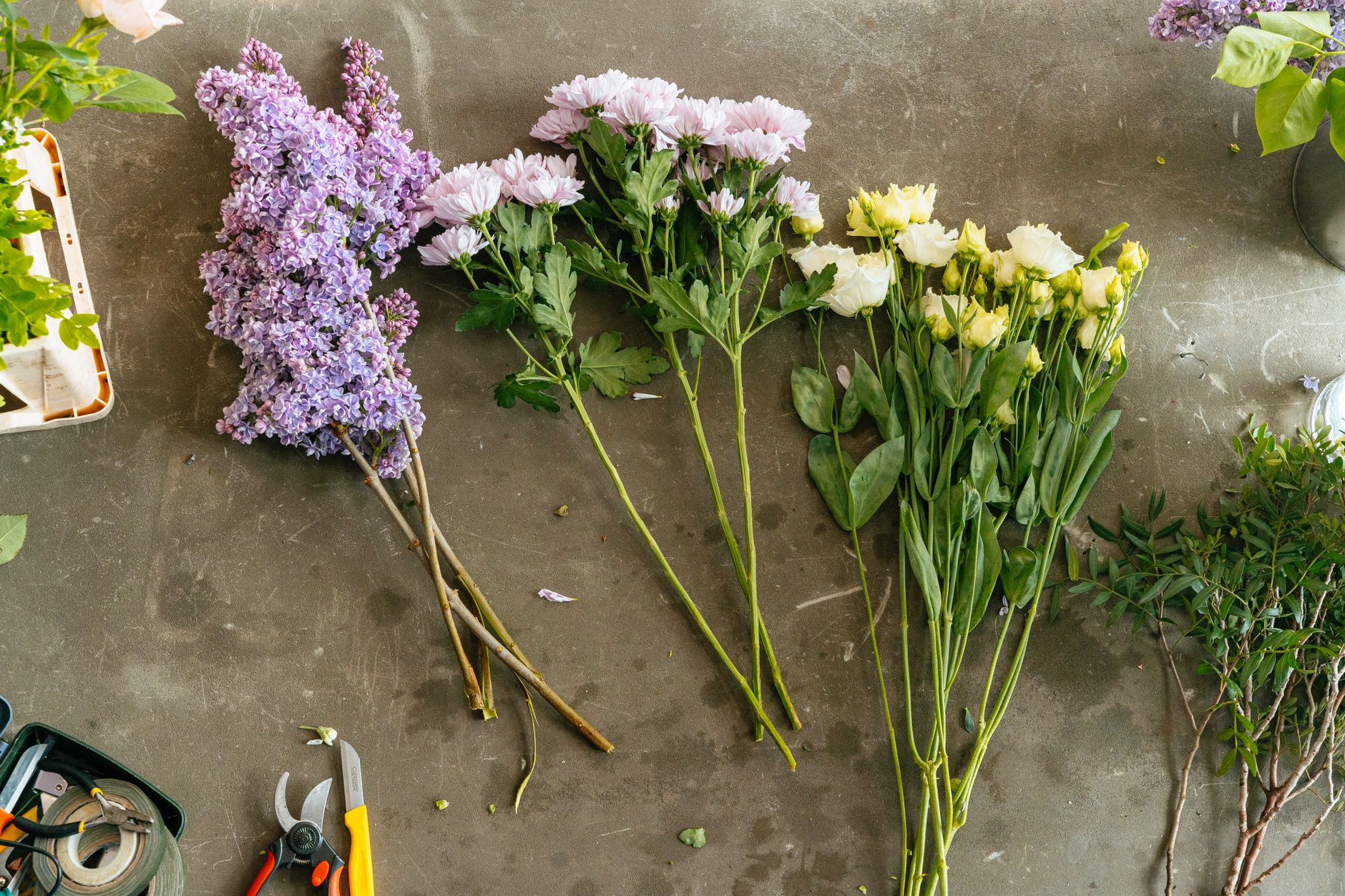 A flat lay of diverse flower arrangements including lilacs and chrysanthemums on a workbench.