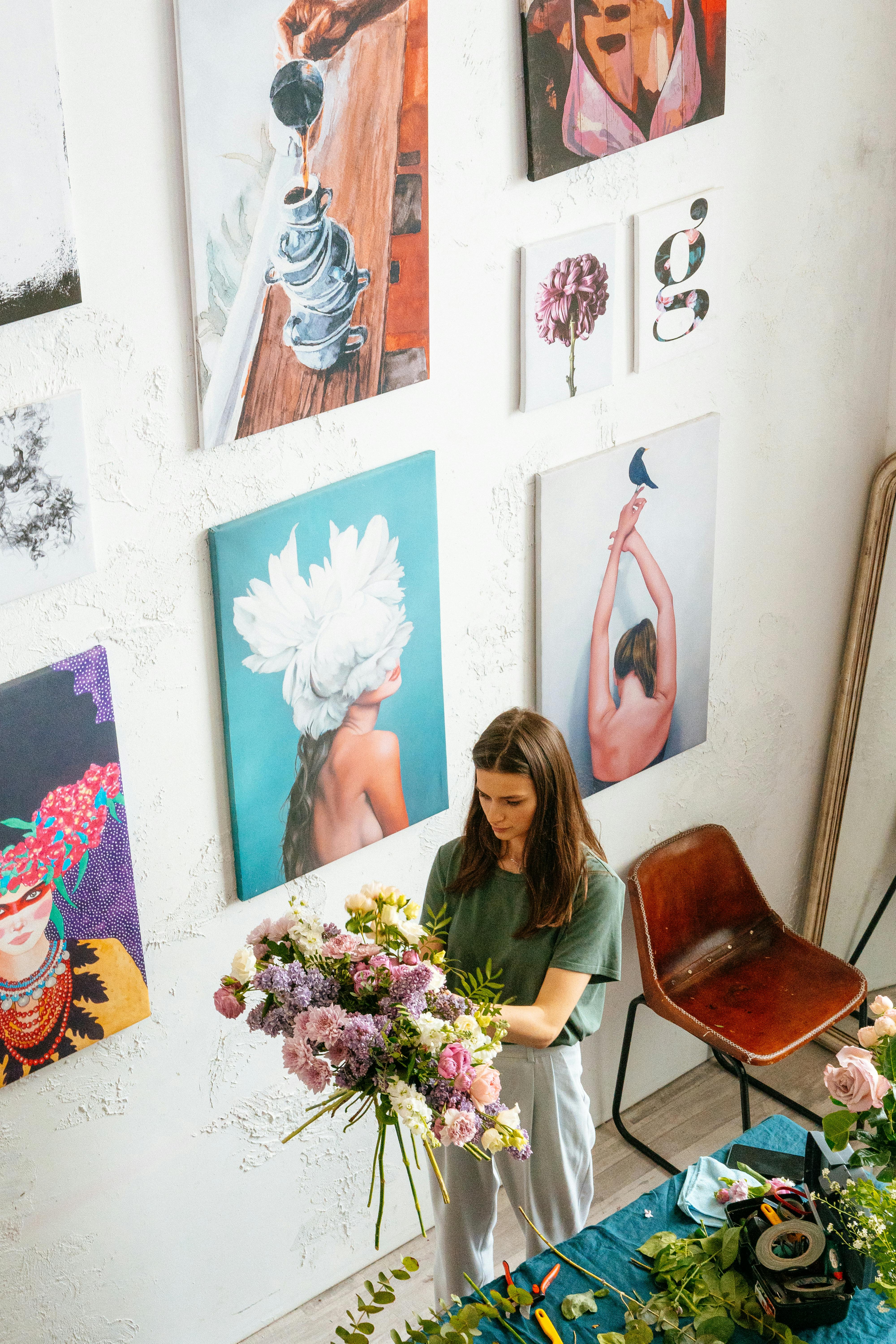 在一家艺术工作室里，一名妇女正在摆放一束鲜花，墙上挂着画作