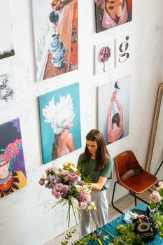 在一家艺术工作室里，一名妇女正在摆放一束鲜花，墙上挂着画作