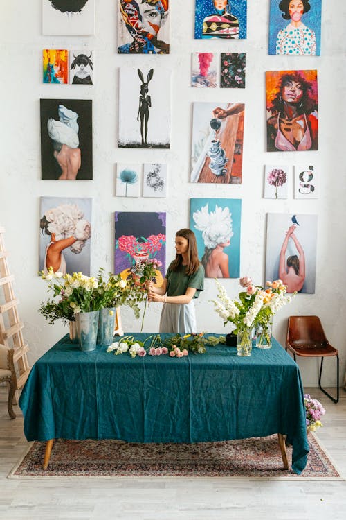 A Woman Holding Flowers While Standing Near Wall with Paintings