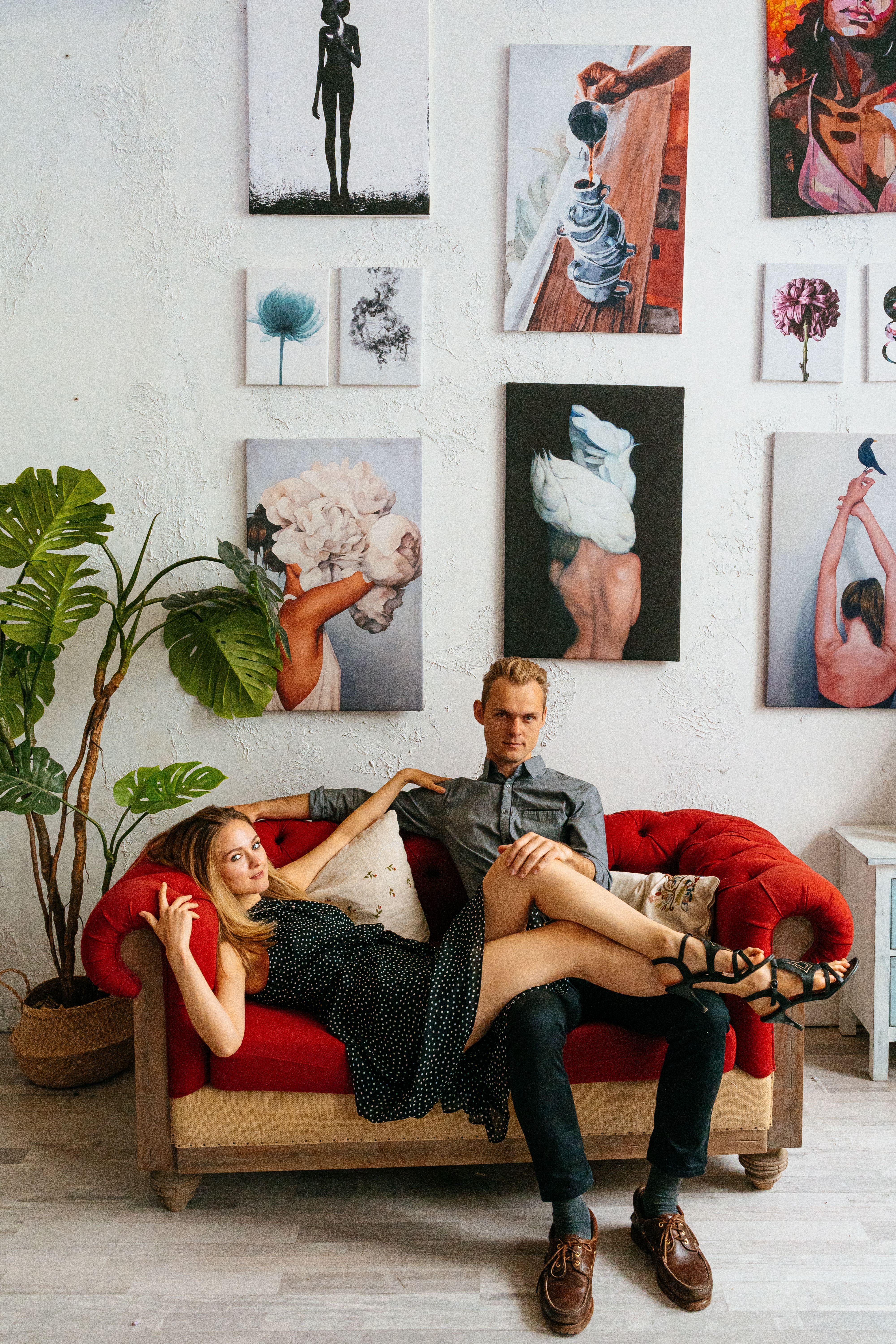 A young couple lounging on a red sofa in an art studio with modern paintings.