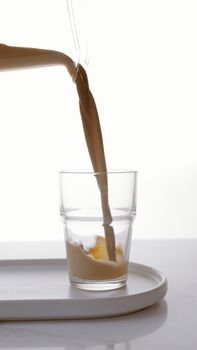 特写镜头中，牛奶被倒入白色托盘上的玻璃杯，简约而干净