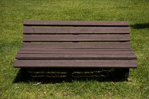 Free A wooden bench on a lush green lawn, perfect for outdoor relaxation. Stock Photo